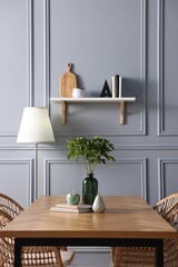 Vase with green branches, books and decor on wooden table in stylish dining room