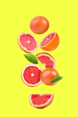 Fresh ripe grapefruits and green leaves falling on yellow background