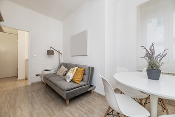 A small living room with a sofa bed upholstered in gray velvet and a white circular table with matching chairs