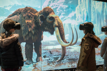 A young, curious child is immersed in a prehistoric world through virtual reality, standing in awe before the towering skeletons of ancient dinosaurs on display.