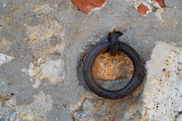 Clappers on an ancient stone wall. Old iron circle to hang boats on the dock.