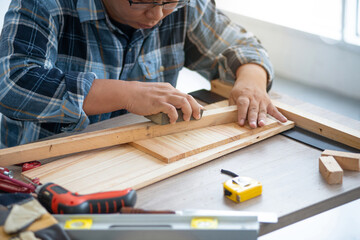 Asian male using sandpaper for polishing wooden, carpenter doing his job in carpentry workshop - obrazy, fototapety, plakaty