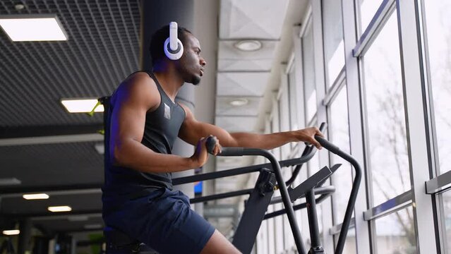 Athletic man doing intense workout on air bike in modern gym
