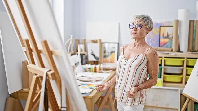 A mature woman artist painting on canvas in her bright art studio, reflecting creativity and education.