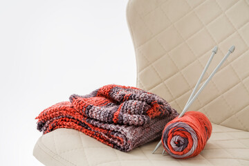 A ready-made knitted set and knitting needles stuck in a skein of yarn are folded on a chair