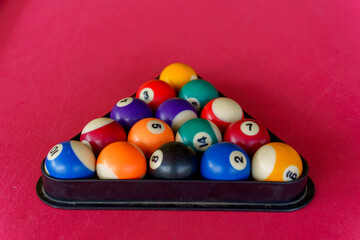Multi-colored snooker balls in a black triangle frame on a red cloth background.