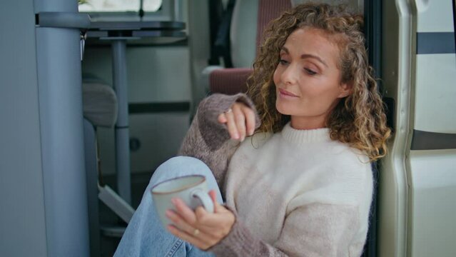 Serene woman enjoy morning beverage sitting campervan stairs in sweater close up