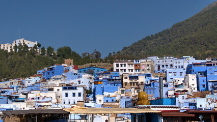 Fototapeta na wymiar Blue and white houses in a hill in the medina, in Chefchaouen, Morocco, with mountains rising up in the background