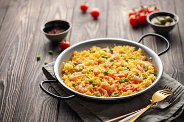 Traditional spanish seafood paella with rice, shrimps, olives and green peas in paellera on wooden...