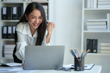 Asian businesswoman, office worker happy and cheerful while receiving recognition on laptop computer, expressing excitement over success and company annual bonus. Success concept.