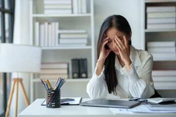 Asian businesswoman is tired, headache, sleepy and bored from sitting at a desk for a long time working on a laptop computer. Problematic financial paperwork Office syndrome concept.