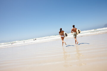 Couple, beach and surfboard for surfing or running with tide check, adventure and fitness with blue sky. Man, woman and surfer by ocean in the morning for holiday, vacation and freedom with rear view