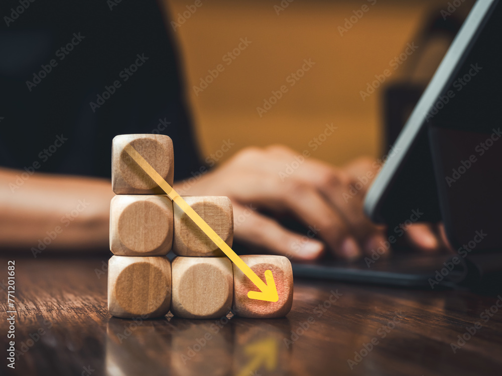 Aufkleber soaring down arrow on wooden blocks as business graph step on table with businessman working with la