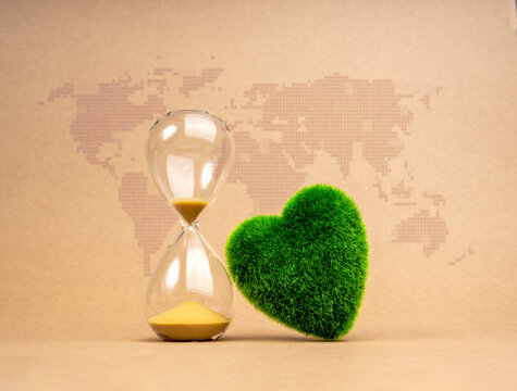 Green life sustainability, environment responsibility concept. Last chance for restoring the earth. Green grass heart shaped and hourglass isolated on digital world map and recycle paper background.