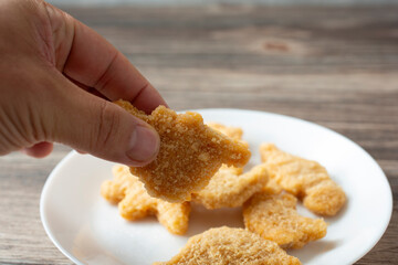 A view of a hand picking up a dino nugget from a plate.