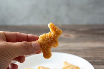 A view of a hand picking up a dino nugget from a plate.