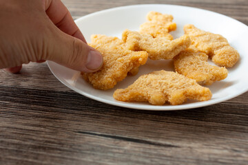 A view of a hand picking up a dino nugget from a plate.
