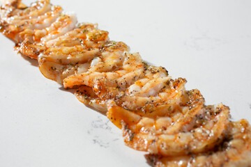 A view of a diagonal row of skewered cooked shrimp, against a white background.