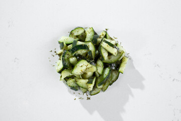 A top down view of a pile of chopped seasoned cucumbers, against a white background. 