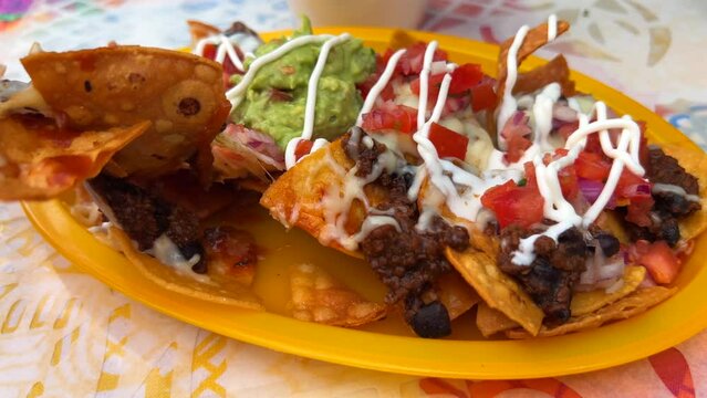 Eating traditional Tex-Mex Mexican nachos with beef chilli con carne, guacamole, melted cheese and sour cream, totopos tortilla chips, tasty food, 4K shot
