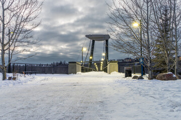 Fort Edmonton foot bridge in night light with dark sky clouds and snow cover