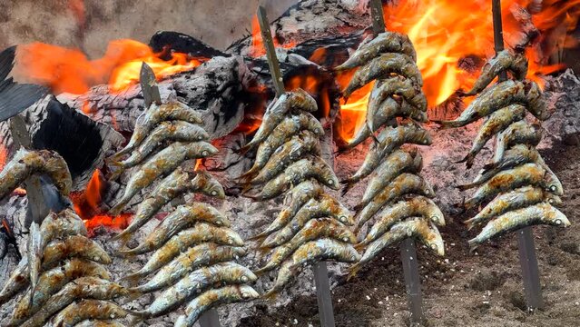 Traditional Spanish sardines Espetos fish grilled at the beach over fire on metal skewers in Marbella Malaga Spain, delicious seafood, 4K shot