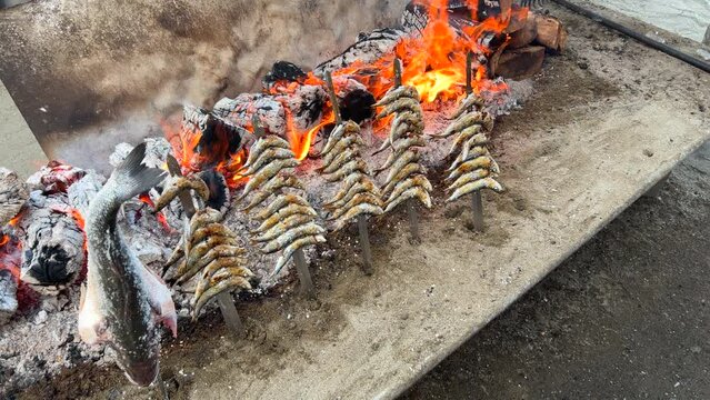 Traditional Spanish sardines Espetos fish grilled at the beach over fire on metal skewers in Marbella Malaga Spain, delicious seafood, 4K static shot