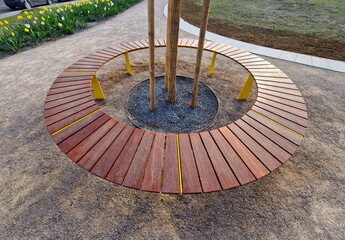 round bench made of wood encloses a tree, sitting around with wood paneling. metal frame. segments...
