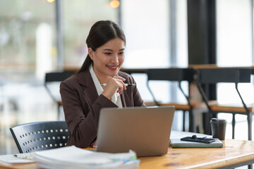 Asian businesswoman sitting and thinking analyze financial reports Business growth using laptop computer and documents, graphs, charts, investment calculators. Office business plan