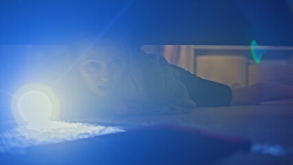 Caucasian teenager comes to modern light room. Young beautiful girl with flashlight tries to find digital tablet computer under big bed in her bedroom. Shooting from under the bed. Lifestyle concept.