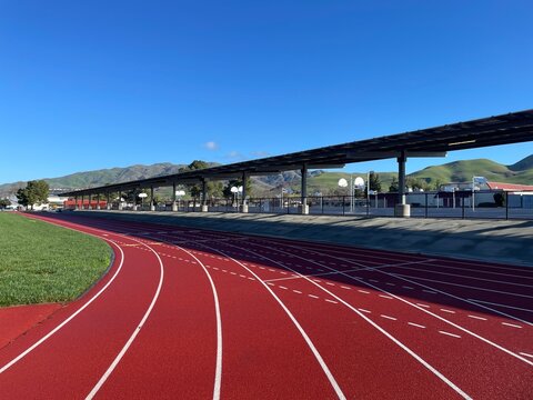 Red Running Track and Lush Green Field with Mountain View and Basketball Court in Serene School Surroundings under Clear Blue Skies
