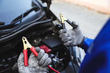 Close-up hand auto mechanic using connect jumper cable on terminal dead battery for jump-start or...