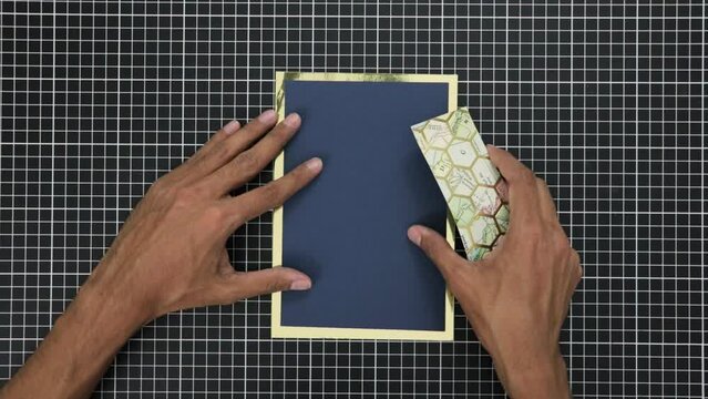 Hands crafting a gift card with gold foil on a gridded cutting mat, overhead view
