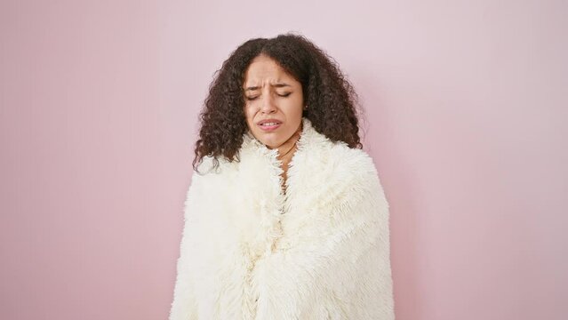 Gorgeous young hispanic woman wrapping in a warm blanket over pink isolated background, feeling freezing cold indoors