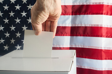 Hand putting his vote into ballot box against national flag of United States - 771258440