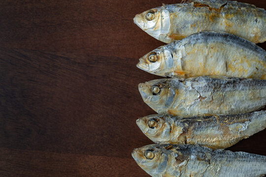 Row of dried herrings on a wooden cutting board.