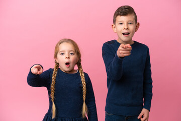 Little caucasian brothers isolated on pink background surprised and pointing front