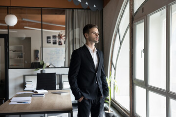 Serious pensive handsome company owner man in formal suit posing in office, looking at window away in deep thoughts, planning future project, thinking on business success, successful work strategy - obrazy, fototapety, plakaty