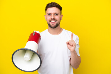 Young caucasian man isolated on yellow background holding a megaphone and pointing up a great idea