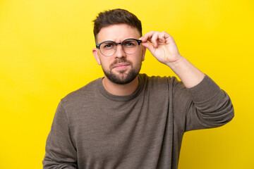 Naklejka premium Young caucasian man isolated on yellow background With glasses and frustrated expression