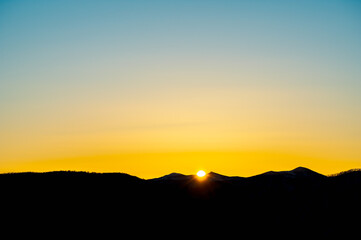 山の稜線から昇る眩しい太陽と美しい朝焼けの空。 - obrazy, fototapety, plakaty