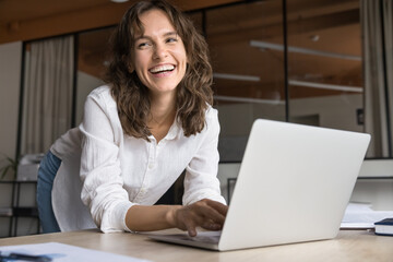 Positive young business woman typing on laptop in office, smiling, laughing, having fun at workplace, looking away, enjoying modern technology, online job communication - obrazy, fototapety, plakaty
