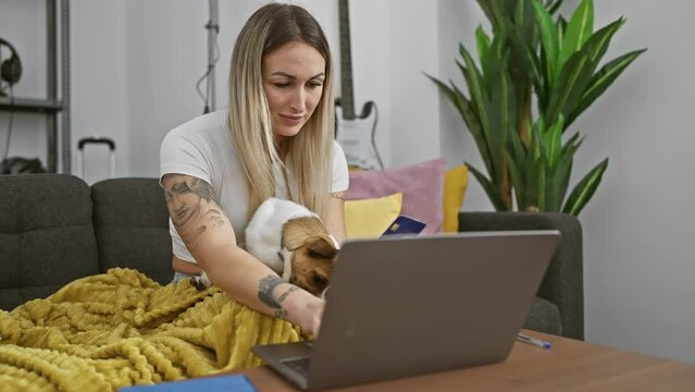 A tattooed woman online shopping with credit card and laptop, accompanied by her jack russell terrier in a cozy home.