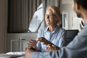 Positive inspired older professional woman speaking at meeting table, talking to business...