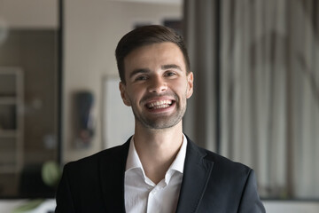 Cheerful handsome business man in formal jacket looking at camera with toothy smile, laughing. Happy ambitious young professional, company CEO head shot online video call portrait - obrazy, fototapety, plakaty