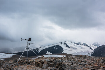 Automatic meteorological station on stone hill with view to large snow-capped mountain range....