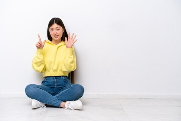Obraz premium Young Chinese woman sitting on the floor isolated on white wall counting seven with fingers