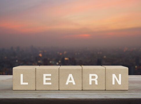 Learn letter on wood block cubes on wooden table over blur of cityscape on warm light sundown, Business, education and learning concept