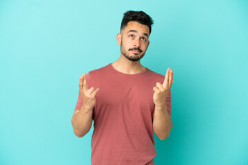 Young caucasian man isolated on blue background with fingers crossing and wishing the best