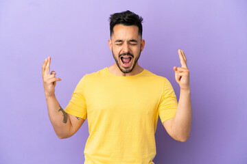 Fototapeta premium Young caucasian man isolated on purple background with fingers crossing